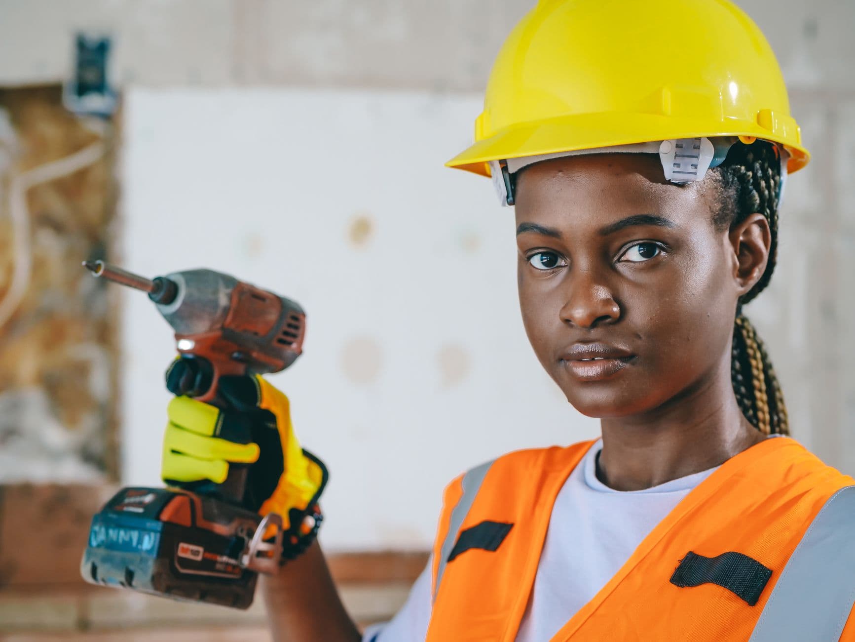 A technician holding a drill, wearing a hard hat and safety vest