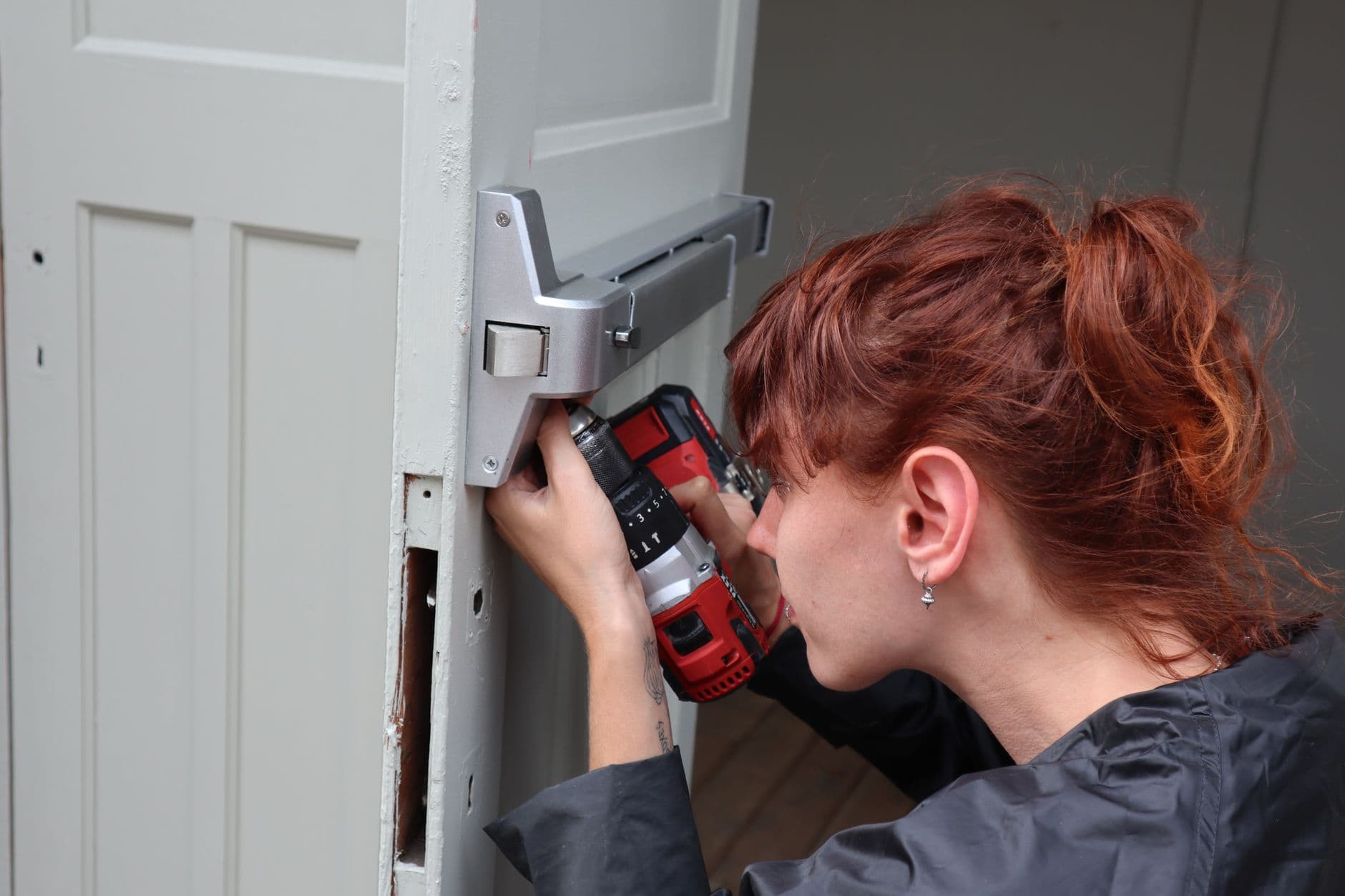 A technician drilling into a door fitted with a panic bar